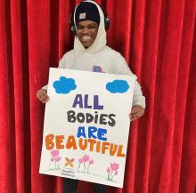 Image of person holding a sign that reads "all bodies are beautiful"